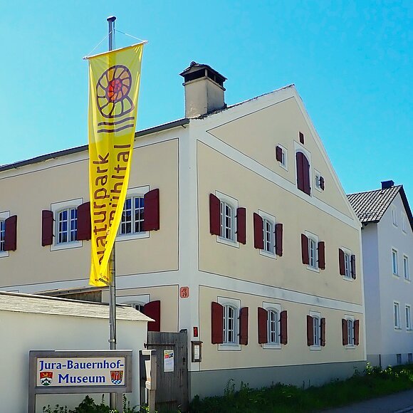 Gebäude mit gelber Flagge "Naturpark Altmühltal" und Schild "Jura-Bauernhof-Museum" davor.