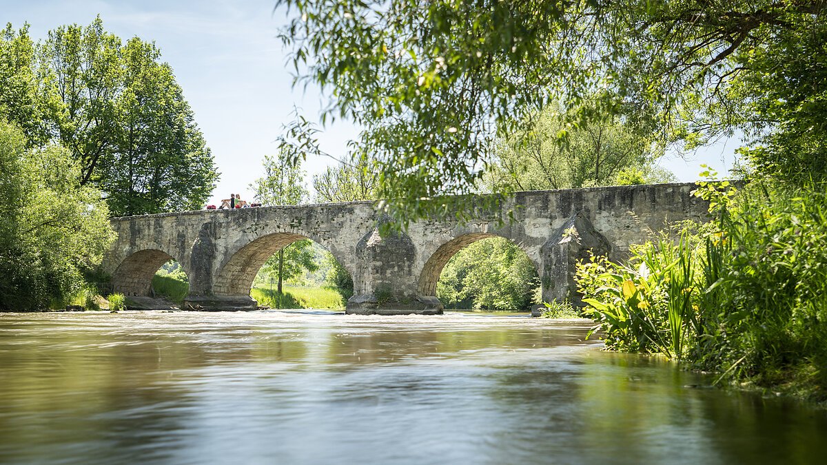 Römerbrücke Pfünz Auf der Römerbrücke sitzen zwei Wanderer Rücken an Rücken auf dem Steingeländer der Brücke. Eingerahmt von Bäumen und unter ihnen die Altmühl.